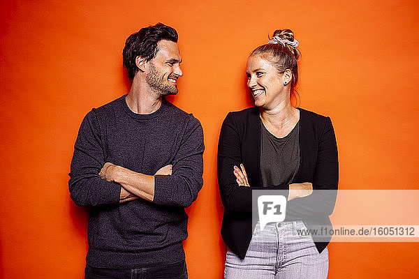 Glückliche Mitte erwachsenen Paar Blick auf einander  während stehend mit gekreuzten Armen gegen orange Hintergrund