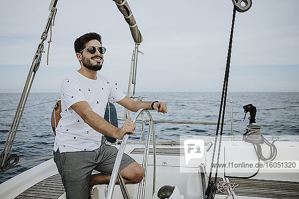 Young sailor wearing sunglasses driving sailboat against sky
