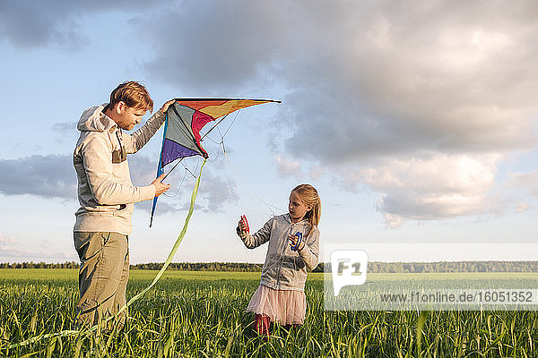 Vater und Tochter lassen einen Drachen steigen  während sie auf einer grünen Landschaft vor dem Himmel stehen