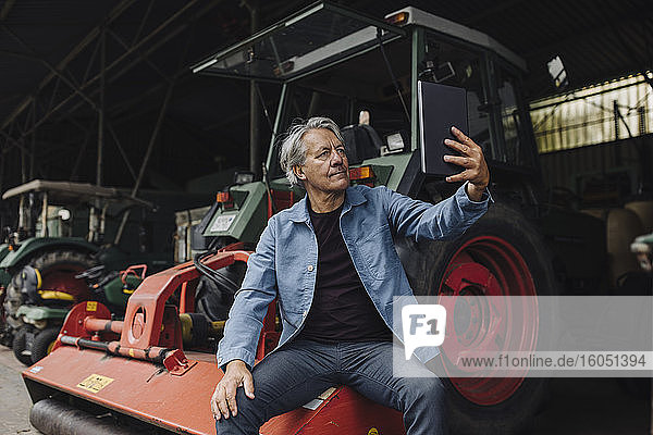 Senior man using tablet on a farm with tractor in barn