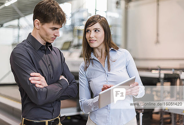 Businesswoman showing digital tablet to male colleague while standing in factory