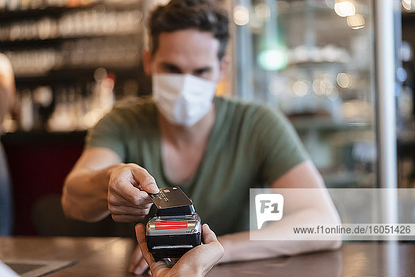 Mann mit Schutzmaske bezahlt mit Kreditkarte in einem Restaurant