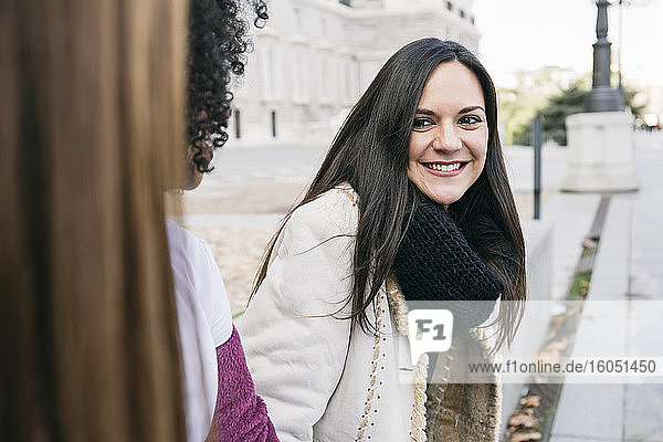 Smiling woman looking at female friends while sitting in city
