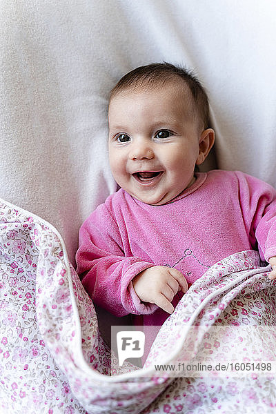 Porträt eines glücklichen kleinen Mädchens im rosa Pyjama auf dem Bett liegend