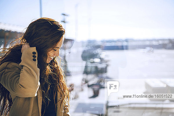 Glückliche Geschäftsfrau mit Hand im Haar  die im Abflugbereich des Flughafens wartet