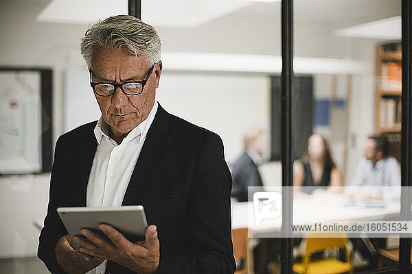 Älterer Geschäftsmann mit digitalem Tablet  Mitarbeiter arbeiten im Hintergrund