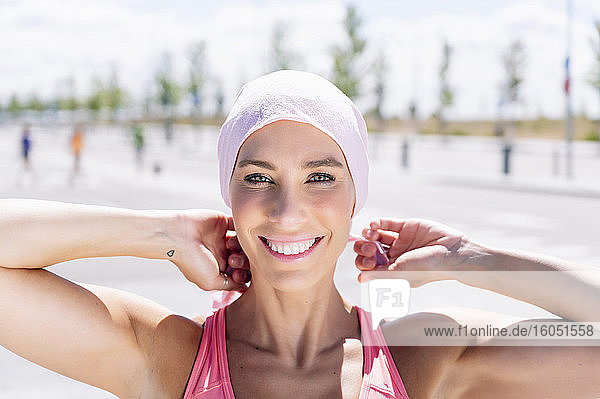 Glückliche sportliche Frau bindet Kopftuch auf der Straße