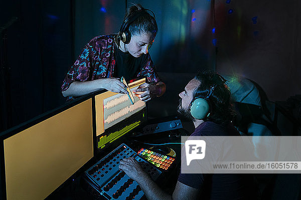 Frau zeigt einem Mann  der einen Computer im Aufnahmestudio zu Hause benutzt  sein Smartphone