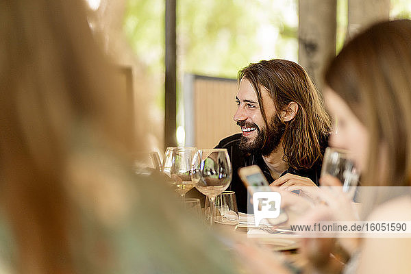 Lächelnder junger bärtiger Mann sitzt mit Freundinnen im Restaurant