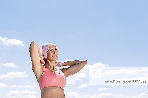 Sportliche Frau mit Kopftuch im Stehen vor blauem Himmel