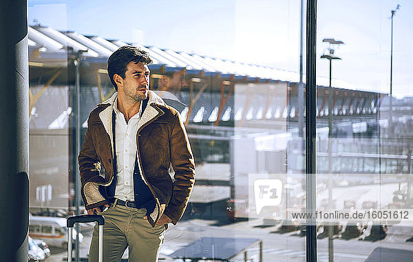 Thoughtful businessman standing with hands in pockets by window at airport departure area