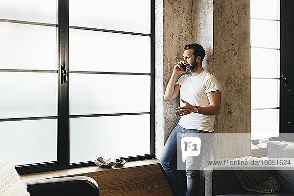Mature man standing by window  using smartphone