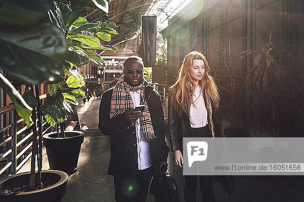 Stilvoller Geschäftsmann  der sein Smartphone benutzt  während er mit einer Kollegin auf dem Gehweg spazieren geht