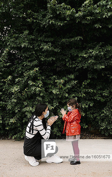 Mutter und Tochter tragen Masken und spielen im Freien ein Klatschspiel