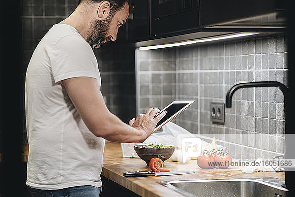 Reifer Mann in der Küche stehend  Essen zubereitend  mit Online-Rezept