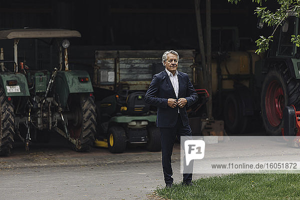 Älterer Geschäftsmann auf einem Bauernhof mit Traktor in einer Scheune