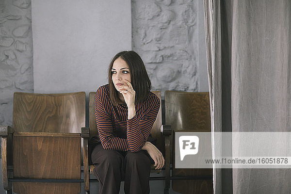 Nachdenkliche junge Frau sitzt auf einem Stuhl in einem Atelier für Bekleidungsdesign