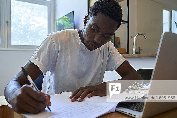 Nahaufnahme eines jungen Mannes  der seine Notizen in ein Buch auf dem Tisch zu Hause schreibt