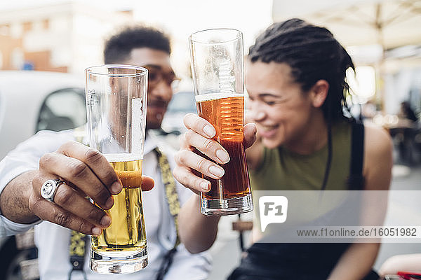 Glückliches junges Paar stößt im Freien an einer Bar mit Biergläsern an