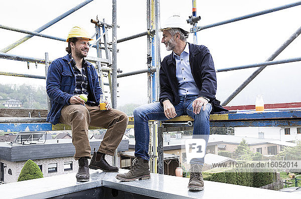 Architect and construction worker talking while sitting at construction site