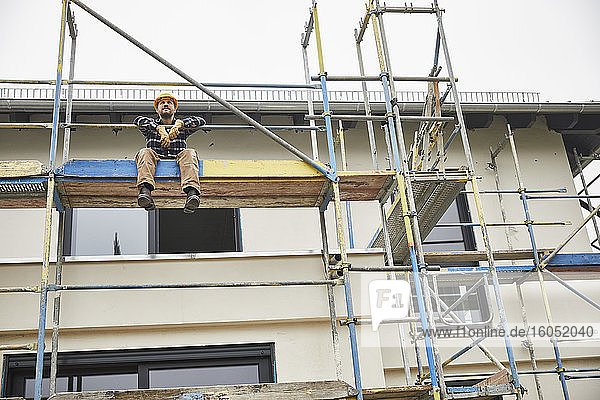 Worker having a break sitting on scaffolding on a construction site