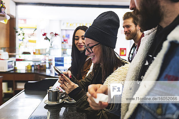 Smiling woman using smart phone while enjoying with friends in cafe