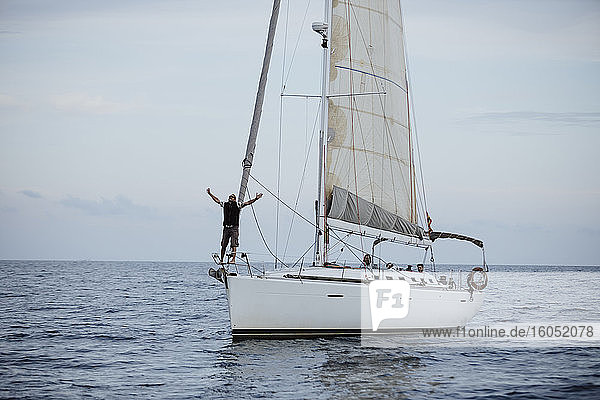 Weiblicher Segler mit erhobenen Armen auf einem Segelboot im Meer stehend