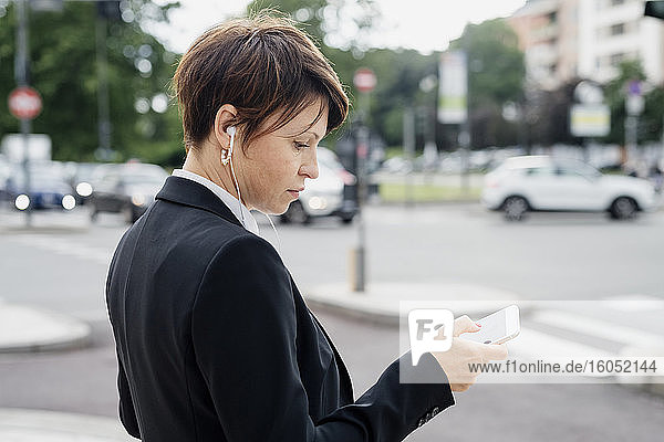 Nahaufnahme eines weiblichen Berufstätigen  der ein Smartphone benutzt  während er auf einer Straße in der Stadt steht