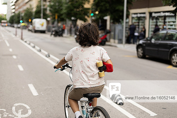 Boy holding skateboard while riding bicycle on street