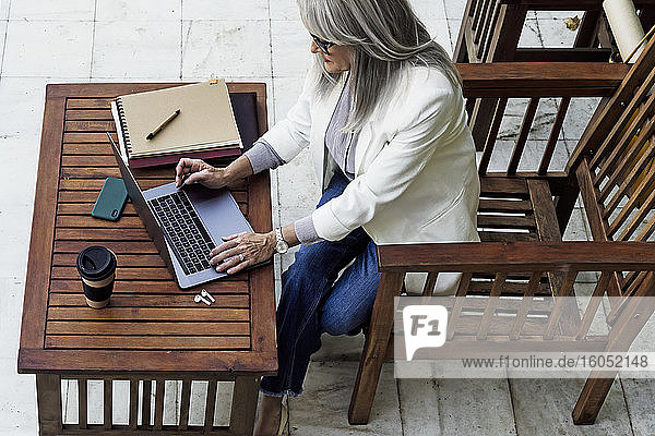 Eine Unternehmerin benutzt einen Laptop und sitzt an einem Holztisch im Garten