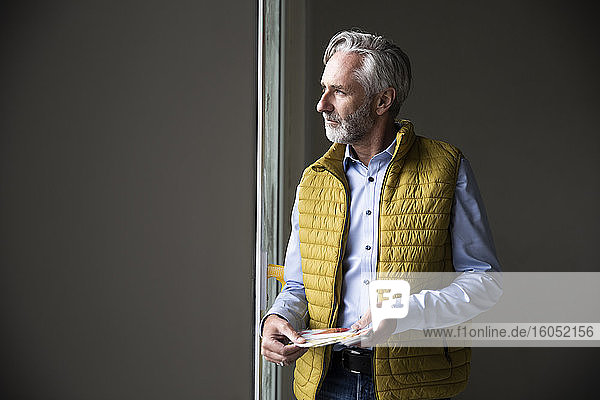 Nachdenklicher männlicher Architekt mit Jacke  der beim Bau eines Hauses durch ein Fenster schaut