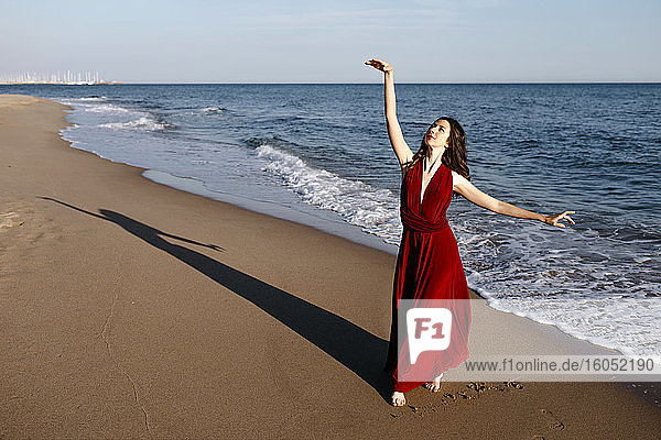 Zarte Frau in rotem Kleid tanzt am Meer  fühlt die Sonne