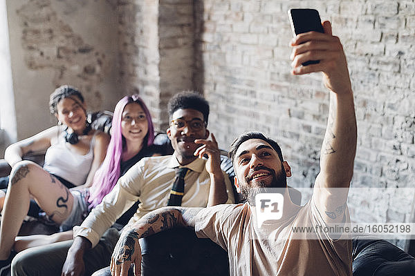 Gruppe von Freunden sitzt auf dem Sofa in einem Loft und macht ein Selfie