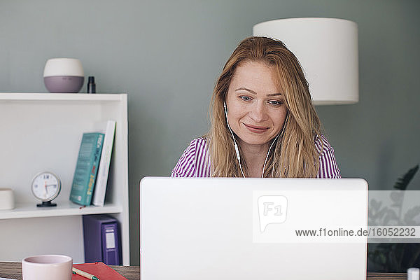 Smiling businesswoman wearing headphones using laptop in office