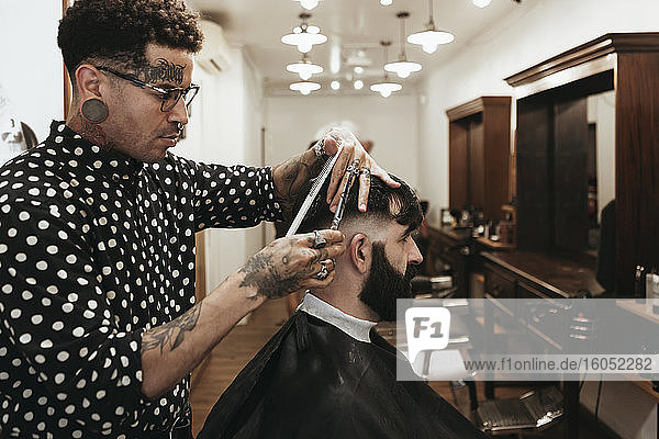Fashionable hairdresser styling man's hair at salon