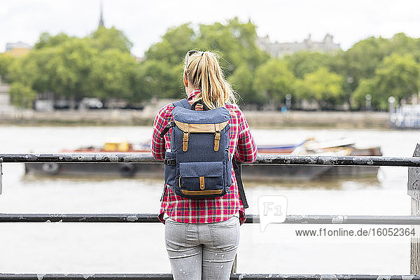 Mid adult woman carrying backpack looking at river while standing by railing