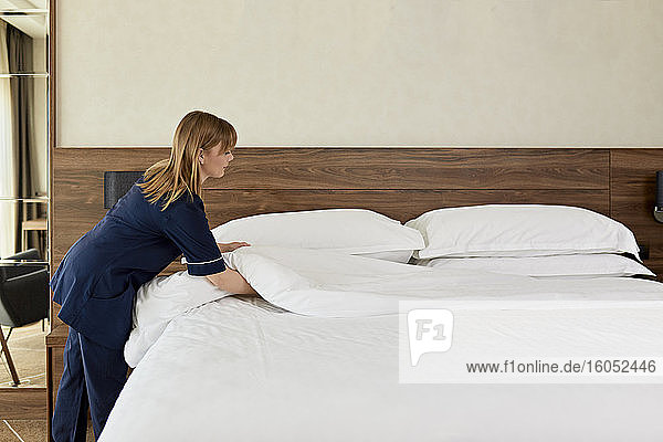 Chambermaid arranging duvet on bed in hotel room