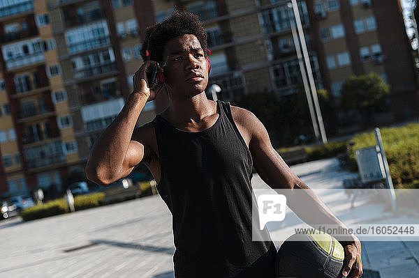 Junger Mann mit Kopfhörern  Smartphone und Basketball in der Stadt