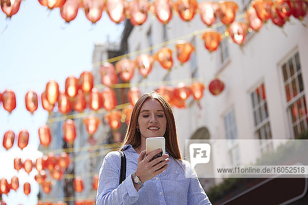 Schöne Frau mit Smartphone unter chinesischen Laternen in der Stadt während des sonnigen Tages