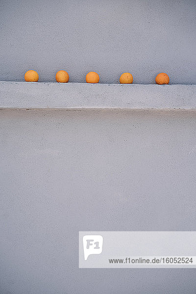 Fünf Orangen auf einem grauen Mauervorsprung