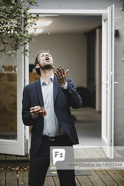 Businessman throwing an eating grapes in backyard