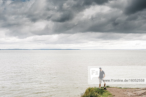 Mann steht auf einer Klippe und blickt auf das Meer vor Gewitterwolken