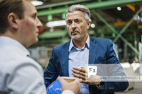 Two businessmen with coffee having a meeting in a factory
