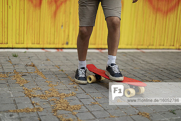 Beine eines Jungen  der auf dem Fußweg Skateboard fährt