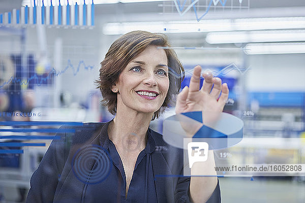 Happy female manager touching line graph on glass in industry
