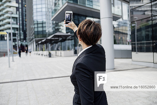 Weiblicher Profi  der ein Selfie mit seinem Smartphone macht  während er vor modernen Gebäuden in der Stadt steht