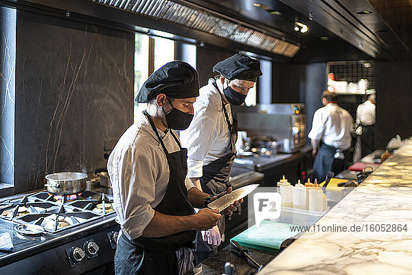 Köche mit Gesichtsschutzmasken arbeiten gemeinsam in einer Restaurantküche