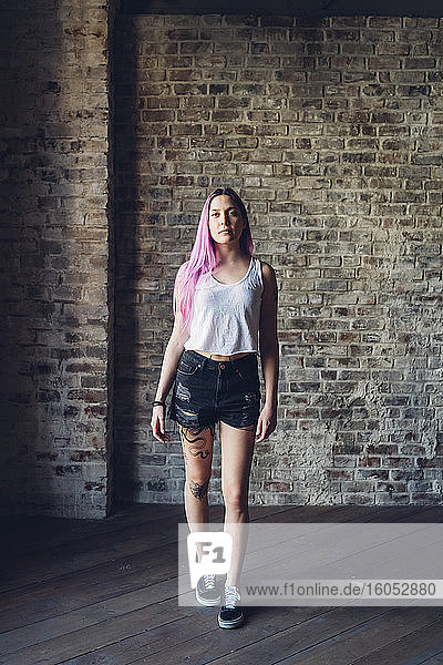 Porträt einer stilvollen jungen Frau mit rosa Haaren in einem Loft stehend