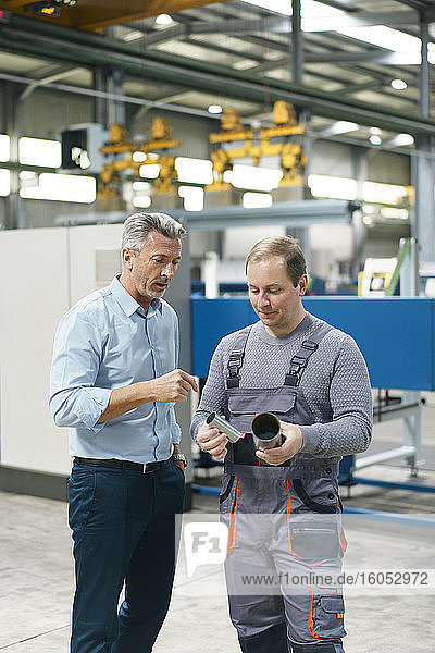 Businessman and worker examining steel pipe in a factory