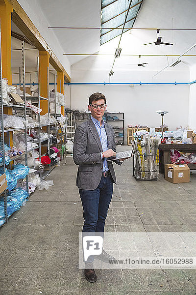 Portrait of a confident businessman holding laptop in a warehouse